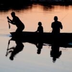 silhouette of three person riding on boat on body of water